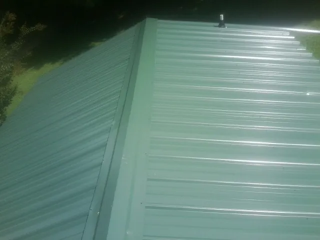New green metal panels meeting at the ridge of a roof — Flat Roof Repair work by our crew in Medina