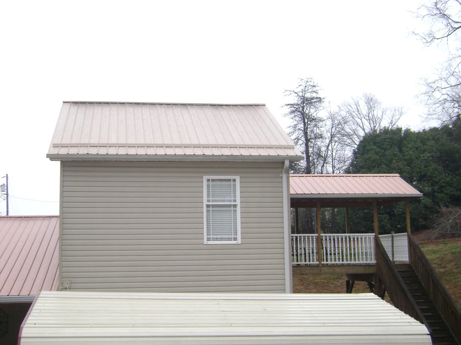 Tan metal roofs on a two story addition and attached porch, from a Roof Replacement job in Medina